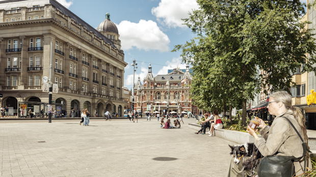 Mensen op het vernieuwde Leidseplein met natuurstenen bestrating en bomen.