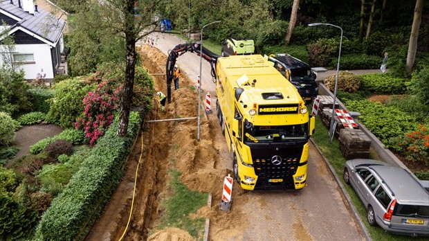 Grondzuigtechniek bij aanleg van kabels en leidingen in woonwijk, met zuigwagen langs open sleuf.