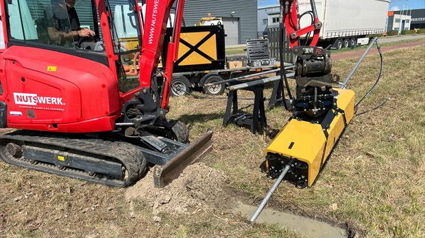 Machinist werkt met rode minigraver en Hydrodrill op veldlocatie