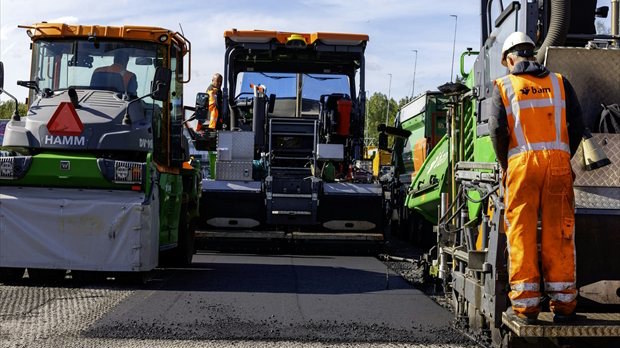 Wegenbouwmachines brengen een nieuwe asfaltlaag met vezels aan op de A10 Oost.