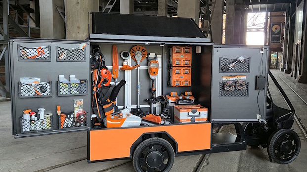 Orange mobile tool workshop on wheels with cabinets open, showing drills, bottles, hoses, and tools organized inside.