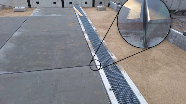 Trench drain with metal grate between concrete slabs at a construction site, channeling surface water.