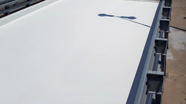 White flat rooftop with metal railing along the edge; a streetlight shadow is cast across the surface.
